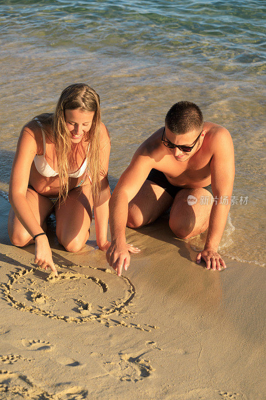 年轻的男女情侣在沙滩上画笑脸。海夏天浪漫
