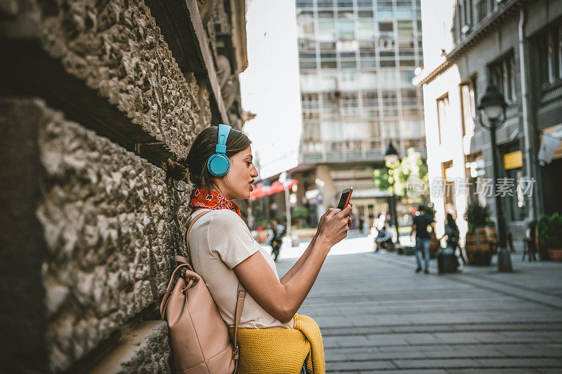 一名年轻女子正带着她的智能手机走在城市的路上