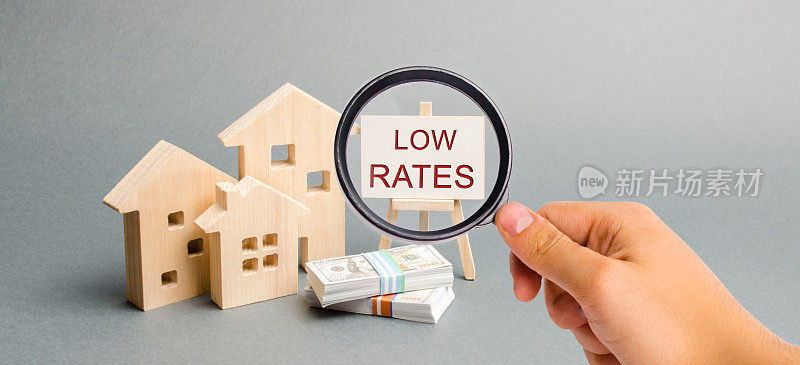 一个放大镜看着一张写着“低利率和木屋”的海报。降低抵押贷款利率的概念。住房信贷。租金。房地产资本化。保险