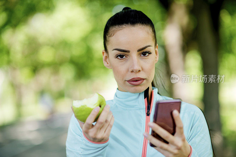 用智能手机吃苹果的女人的肖像