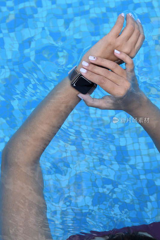 女人的手拿着智能手表在游泳池里