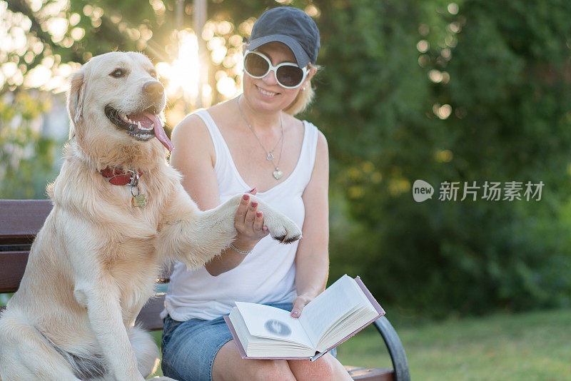 妇女们和她的狗坐在公园的长椅上看书