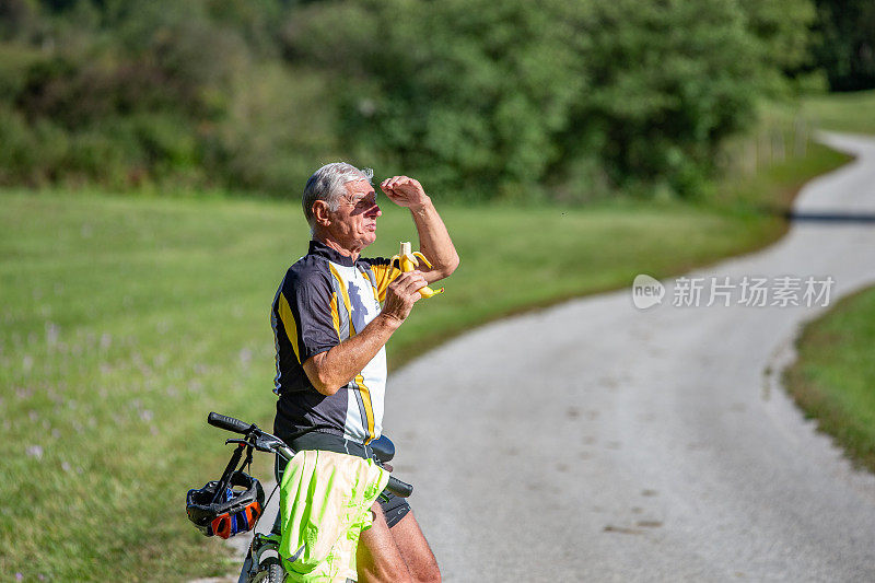 老年骑自行车者在乡村公路上休息和吃香蕉