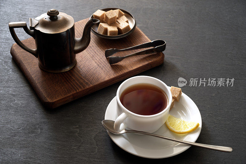 黑木背景上放一大杯红茶，配壶和糖