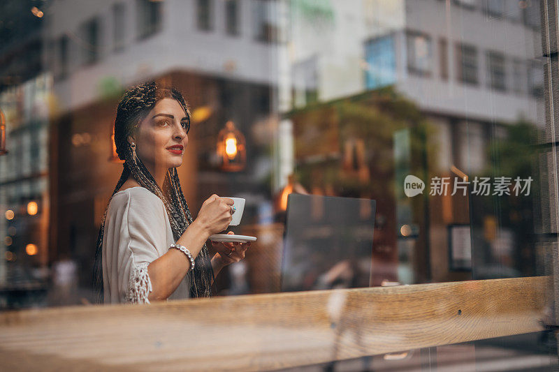 一位女士坐在咖啡休息时间，在市中心的咖啡馆里用笔记本电脑