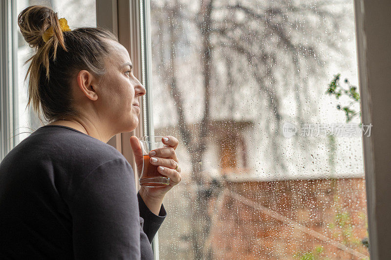 下雨天透过窗户看窗外喝茶的女人