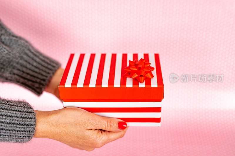 近距离女性的手拿着一个红白条纹礼品盒在粉红色的背景照片