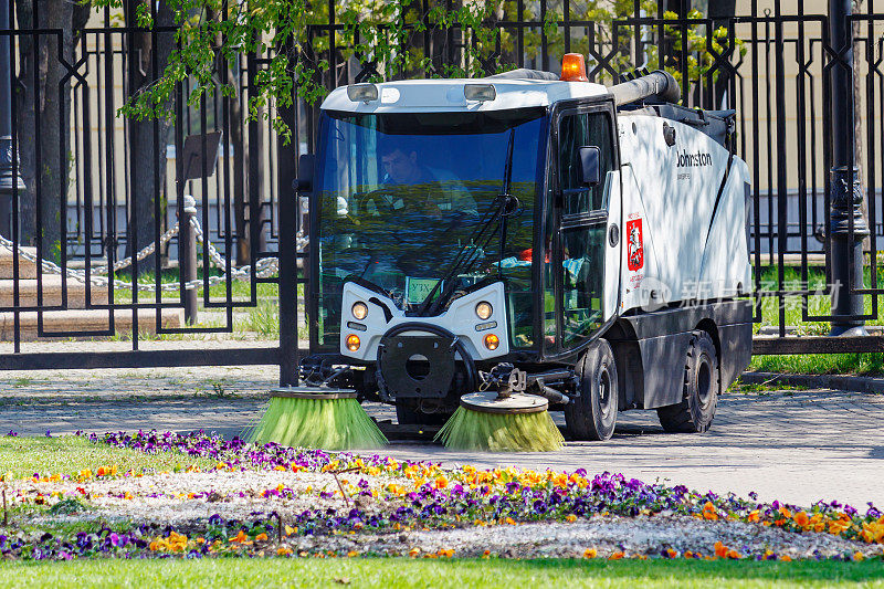 在阳光明媚的春天早晨，小型清扫车清理着城市公园的小路