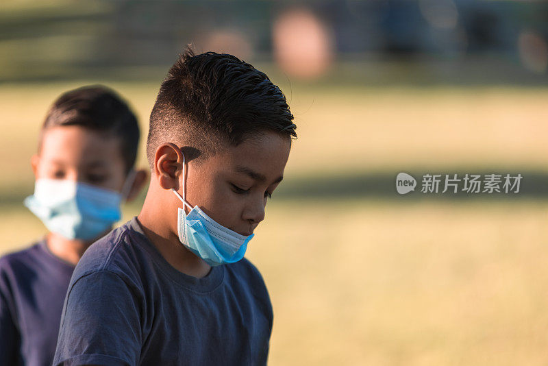 由于新冠肺炎，男孩们戴着防护口罩在公园里下棋、踢足球