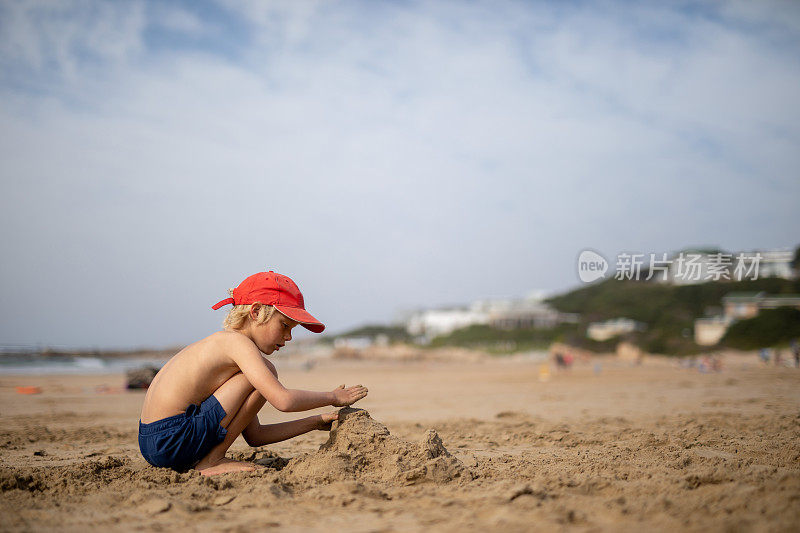 一个小男孩正在沙滩上玩，用沙子建城堡。