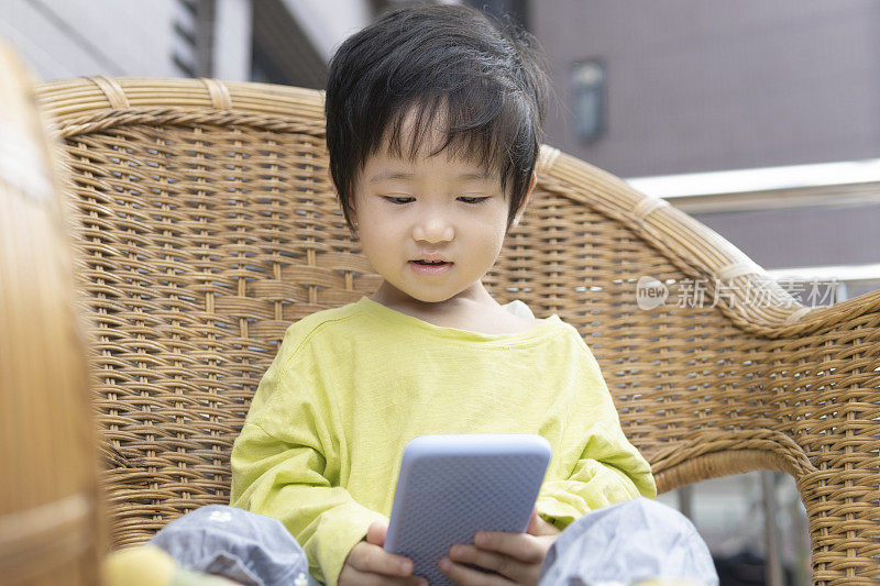 一个中国小女孩在阳台上的藤椅上玩手机