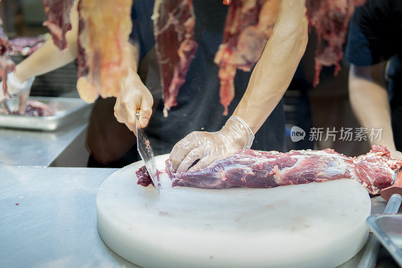 在一家牛肉火锅餐厅的开放式厨房里，厨师在挂着的切碎的生肉后面用刀切牛肉