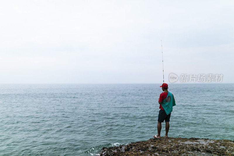 亚洲男子戴着帽子在海滩上钓鱼