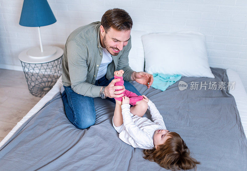 微笑的年轻父亲在给小女儿换尿布的时候和她玩得很开心