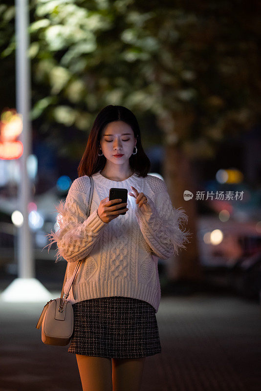 亚洲妇女在夜晚的街道上使用手机
