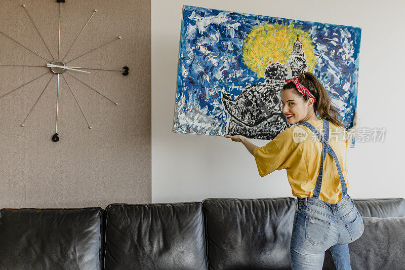 年轻女子把艺术画挂在墙上，装饰客厅
