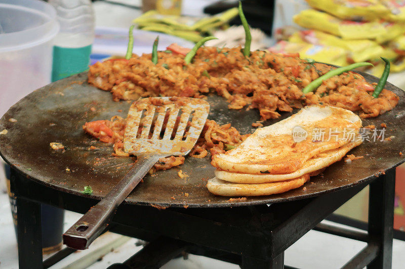 在户外用餐时，用金属锅铲加热着绿辣椒咖喱和印度烤饼面包