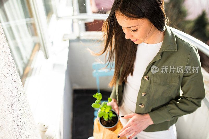 一个年轻女子在她的阳台上捧着一盆植物