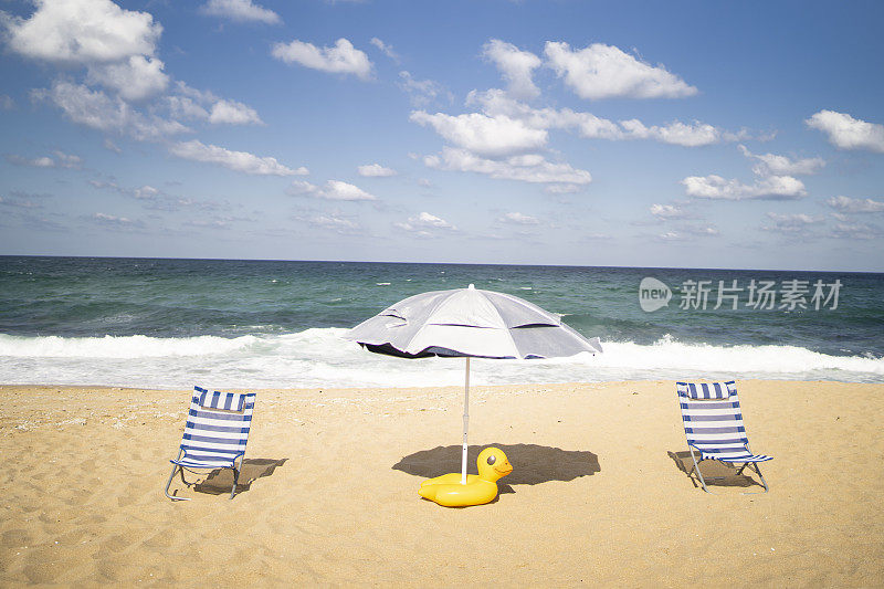 沙滩上有两把沙滩椅，一把阳伞和一只充气橡皮鸭