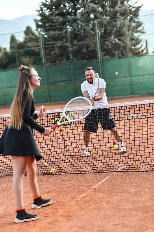 微笑的男网球运动员与女同事在球场上玩耍