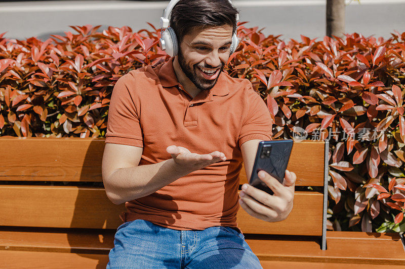 年轻男子微笑着拿着手机，坐在长凳上与某人进行视频通话