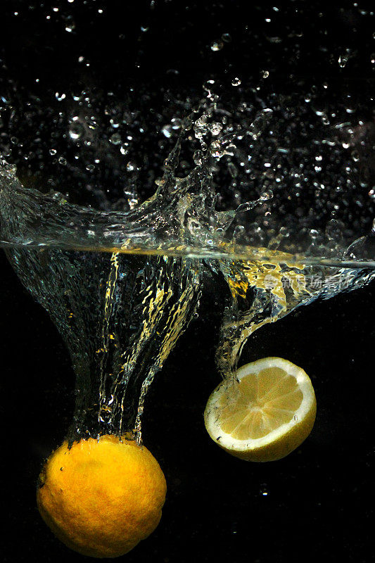 切片柠檬，柑橘水果掉进水里，泡泡和飞溅的水珠在黑色背景下