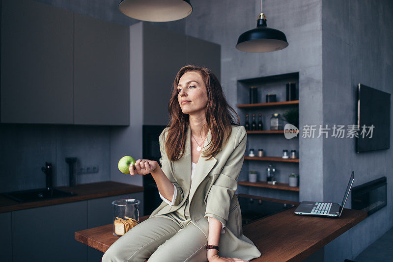 一个女人在休息时拿着一个苹果坐在厨房里