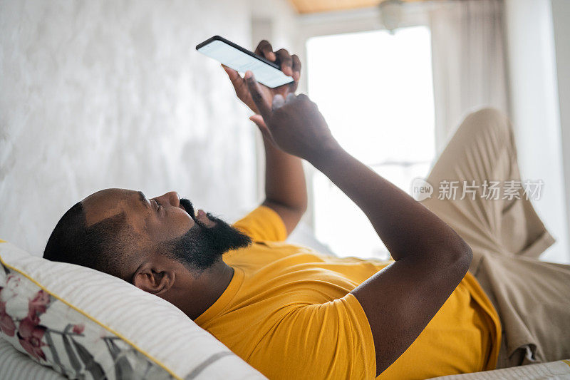 中年人躺在家里的床上玩智能手机