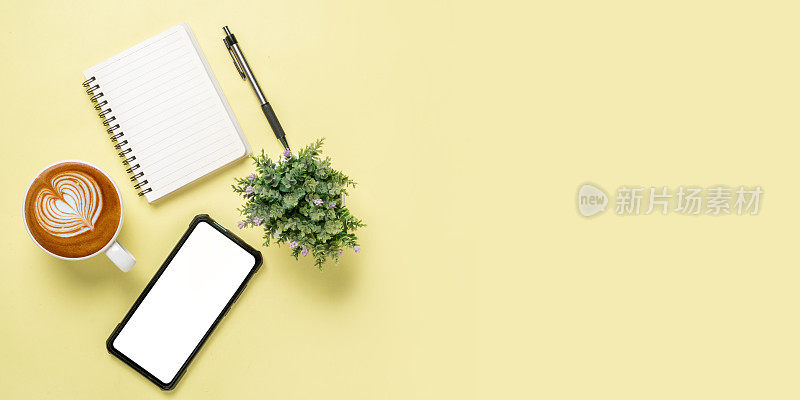 办公室写字台与空白屏幕智能手机，笔，笔记本，咖啡杯黄色背景