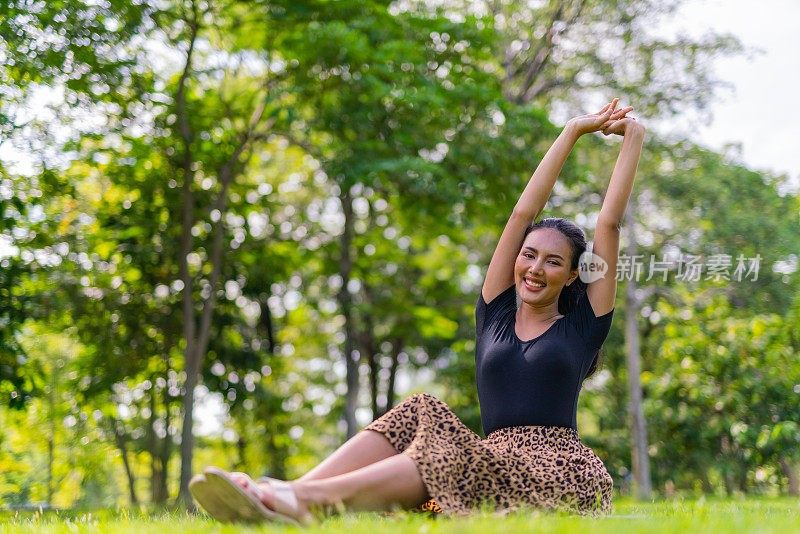 一个美丽的和好看的年轻亚洲女性模特女士穿着夏季寒冷的连衣裙手臂伸展在公园里坐在草地上放松