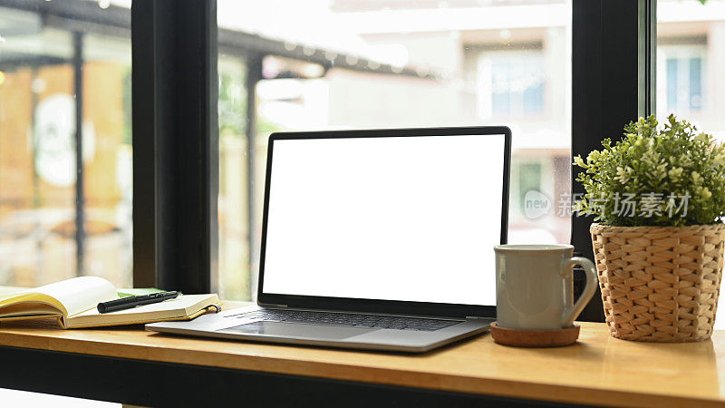 空白显示的笔记本电脑，盆景，咖啡杯和木制桌子上的笔记本电脑。