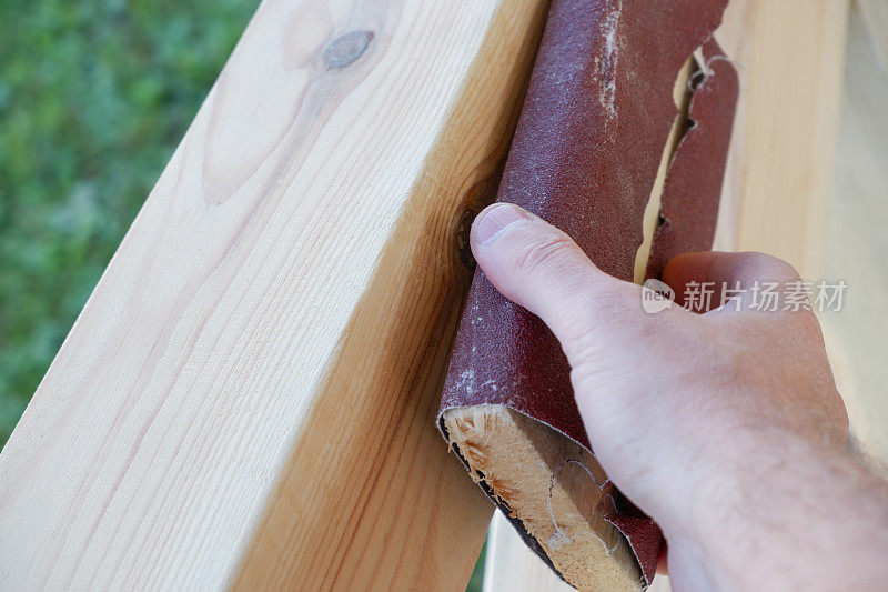 喷砂木头。一位男木匠正在打磨一座人造凉亭的木梁。近距离观察手的木匠摩擦木材与砂纸