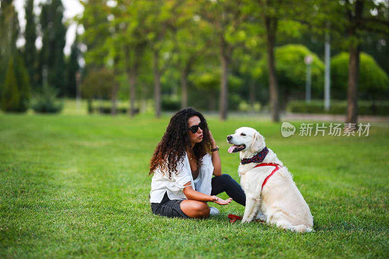 美丽的
深色头发的女人有一个很好的时间和她的金色拉布拉多寻回狗在公园的草地上日落。动物的爱