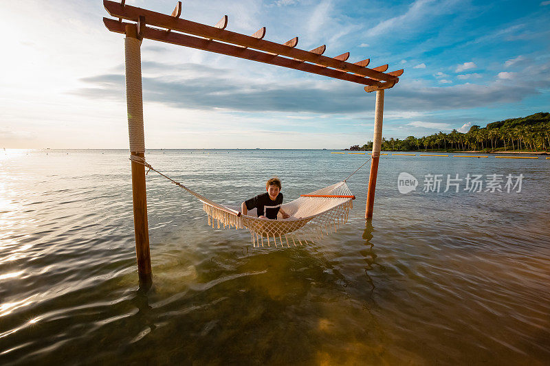 暑假概念，快乐的白人少年在越南热带海滩的海上吊床上放松