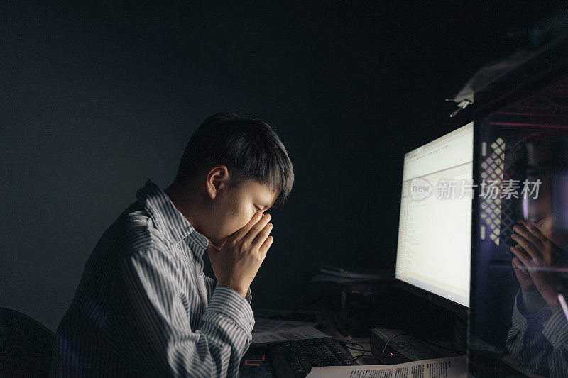 一名亚洲男子看到自己晚上在电脑前被解雇，感到绝望——这是经济低迷时期的生活状况