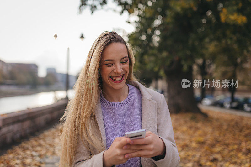 微笑的年轻女子在街上使用智能手机