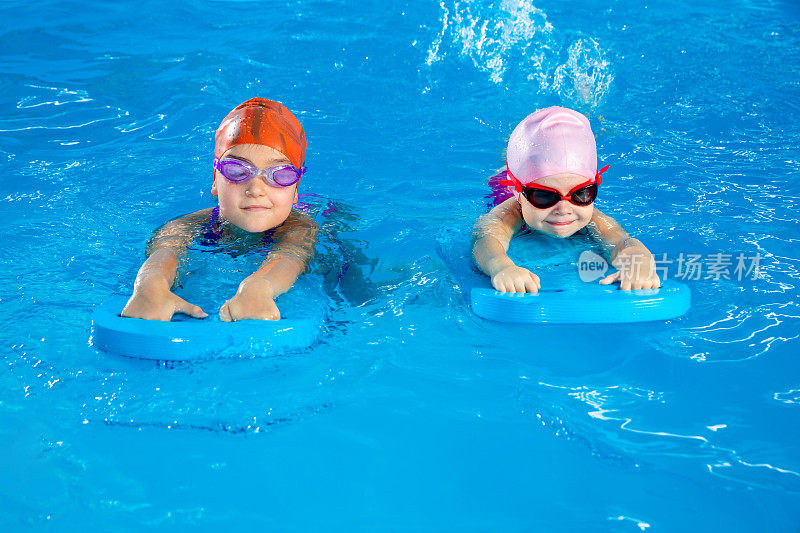 两个小女孩在游泳池里用冲浪板学习游泳
