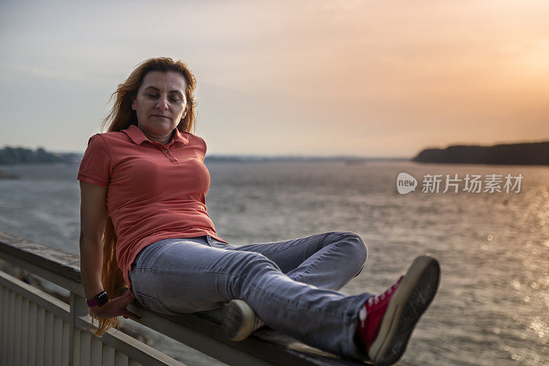 一个40多岁的女人在河边欣赏日落。