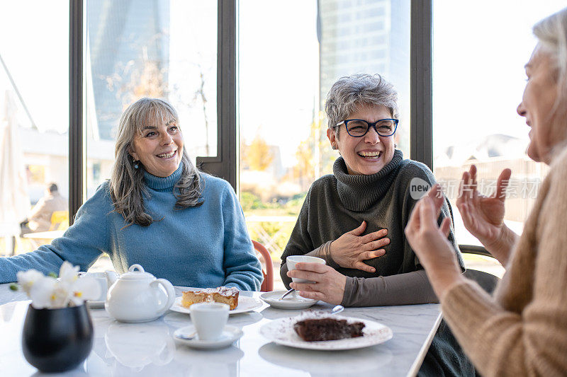 一群老年妇女在自助餐厅吃早餐，三位退休的女性朋友正在喝着茶和咖啡，吃着巧克力蛋糕庆祝周年纪念日