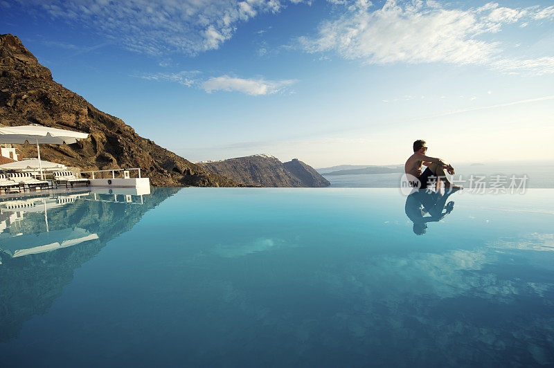 一名男子坐在希腊圣托里尼的无边泳池边缘