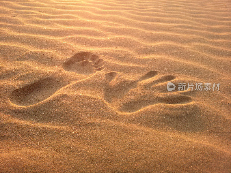 夕阳下沙滩上的手印和脚印