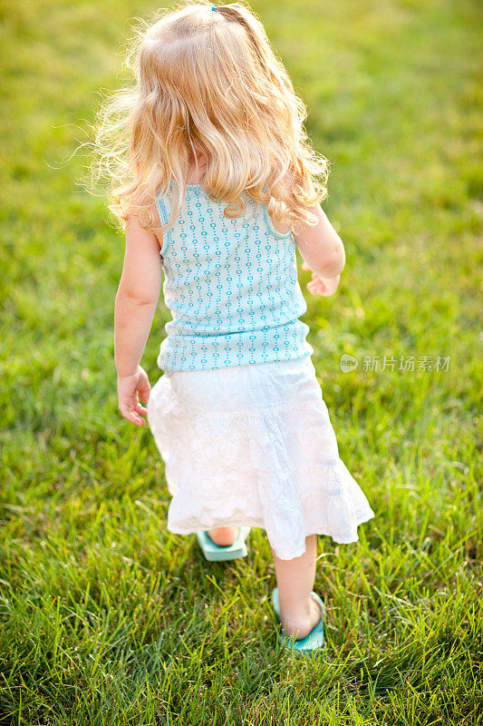 金发小女孩走过外面的草地