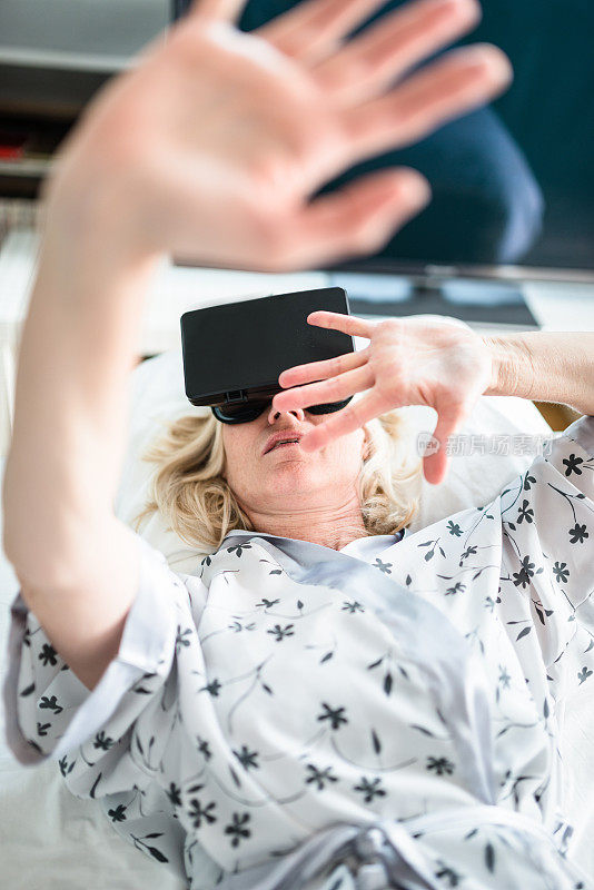 资深女性在床上使用虚拟现实模拟器