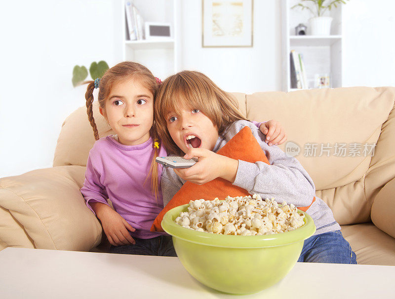男孩和小女孩拿着爆米花看电视