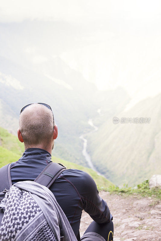 男性徒步旅行者坐着眺望高山和山谷