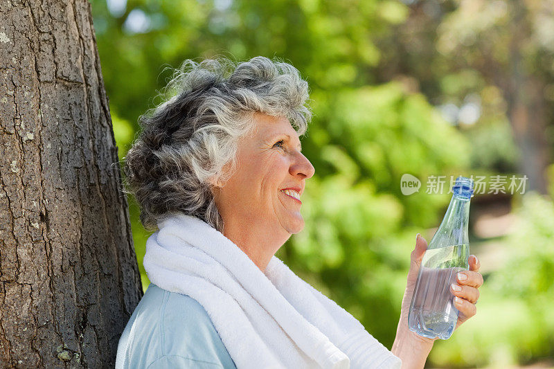 一个女人拿着一瓶水靠在树上休息