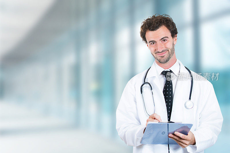 肖像友好的男医生与剪贴板微笑站在医院走廊诊所的窗户背景