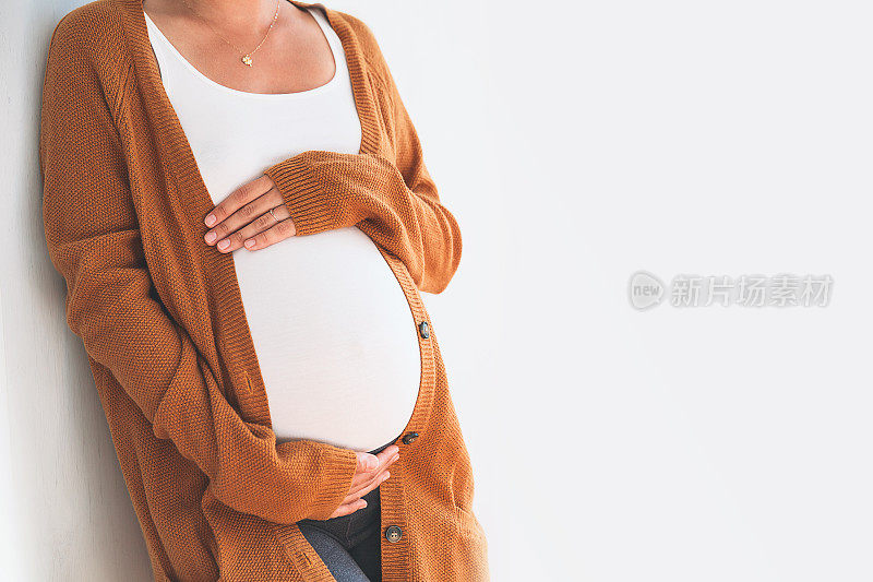 美丽的孕妇用手触摸她的腹部在一个白色的背景。