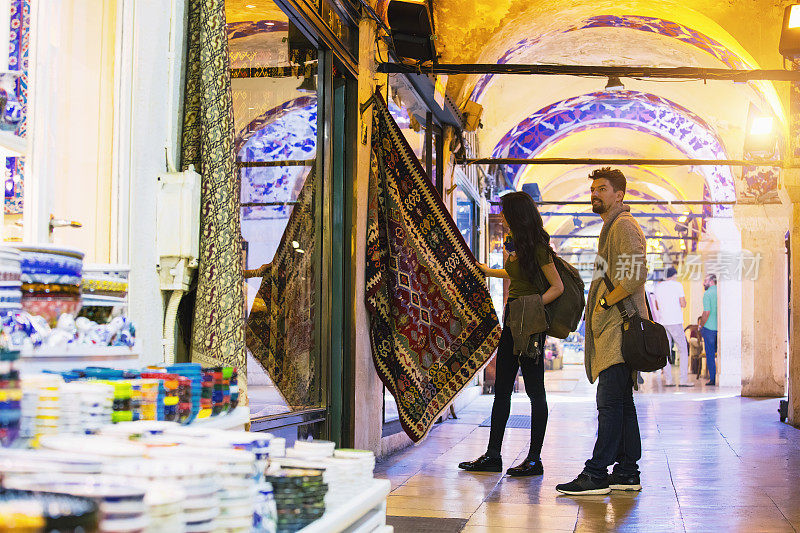 一对年轻的游客夫妇在土耳其伊斯坦布尔的大巴扎购买地毯