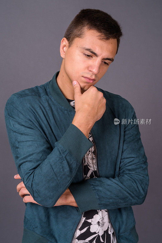 年轻英俊的男子穿着花图案的衬衫和蓝色夹克，以灰色的背景
